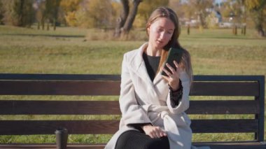 Parktaki bankta oturan genç bir kadın akıllı telefonuyla ateşli video görüşmelerine katılıyor. Sonbahar güpegündüz gergin bir video konuşması sırasında gerginliğini ve endişelerini dile getiriyor.