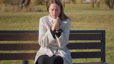 Kadın, soğuk sonbahar gününde ellerini birbirine sürterek parkta tek başına oturuyor. Soğuk hava onu çevrelemiş ve düşen sıcaklıklara karşı mücadelesini vurguluyor.