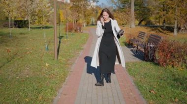 İş kadını elinde kahve fincanıyla sonbahar parkında yürürken hareketli ve hayal kırıklığına uğramış bir telefon görüşmesi yapıyor. Davranışlarındaki sıkıntı ve stresi dile getiriyor.