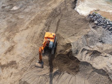 Deniz kıyısında, nehirde ya da barajda çalışan sarı bir kazıcının insansız hava aracı görüntüsü.