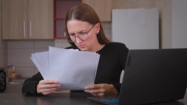 Genç profesyonel kadın dizüstü bilgisayarı üzerinde çalışırken gözlüklerini burnuna sokuyor. Ekranı daha iyi görebilmek için görüşünü geliştirmeye çalışıyor.