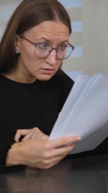 Gözlüklü kadın muhasebeci, evrak okuyor ve masasında dizüstü bilgisayarla çalışırken alnında gözlüklerle geziyor. Belgeleri yönetmede zorluklar yaşıyor.