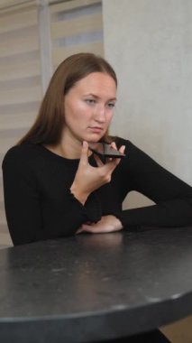 İş kadını masasında oturmuş, akıllı telefonuna sesli mesaj kaydediyor. Siyah balıkçı yaka kazağı giymişti. Sesli iletişimine dikkatle odaklanmıştı. dikey video