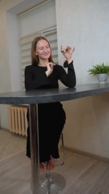 Evinin mutfağında oturmuş gülümseyen genç bir kadın elinde yeni evinin anahtarları, hayatında yeni bir sayfa açmanın heyecanı ve ev sahipliğinin neşesini kucaklıyor.