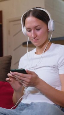 Genç bayan oturma odasında kanepede otururken akıllı telefon kullanıyor. Kulaklık takıyor ve müzik dinliyor.