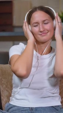 Kanepede oturan, kulaklık takan ve müzik dinleyen genç bir kadın. Gözleri kapalı ve yüzünde gülümsemeyle, elleriyle başını tutuyor, rahatlama ve mutluluktan zevk alıyor.