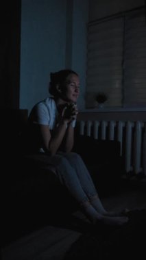 Kanepede oturan genç bir kadın, rahat, loş bir oturma odasında televizyon izlerken heyecanını ve neşesini dile getiriyor, kişisel eğlence ve boş vakitlerin tadını çıkarıyor.