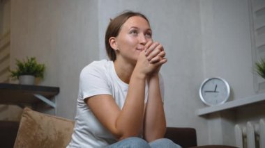 Genç kadın kanepede oturuyor, rahat bir şekilde televizyon izlerken heyecan ve neşe ifade ediyor, akşamları oturma odasında, kişisel eğlence ve eğlencenin tadını çıkarıyor.