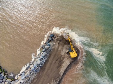 Deniz kıyısında, nehirde ya da barajda çalışan sarı bir kazıcının insansız hava aracı görüntüsü.