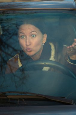 Araba süren şaşırmış bir kadın, şok olmuş bir ifadeyle ön camdan bakar, yoldaki beklenmedik bir olaya tepki verir. Dikey fotoğraf