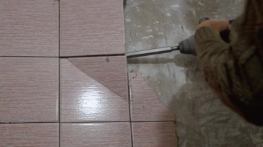 İnşaatçılar eski pembe duvar fayanslarını keski ve çekiçle kaldırarak, yenilenme projesi kapsamında yeni fayanslar döşenmesi için kaba duvar hazırlıyorlar. Toz ve enkaz süreç boyunca havayı doldurur