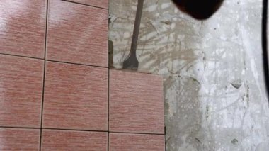 İnşaat işçisi kaya matkabını kullanarak banyo duvarındaki fayansları söküyor. Duvar kısmen yıkılmış, alttaki betonu ortaya çıkarıyor.