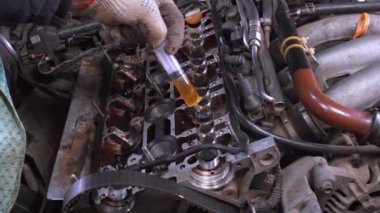 Eldivenli tamirci, araba motorunun şaftına şırıngayla motor yağı döker. Bu süreçte, araba garajında ana bakım ve onarım yöntemleri vurgulanır