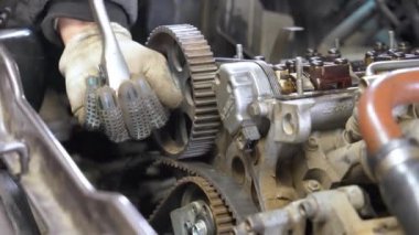 Eldivenli tamirci, İngiliz anahtarı kullanarak araba motorunda zamanlayıcı kemerini sıkılaştırıyor. Araçların onarımı ve bakımında hassasiyet ve vasıflı çalışmalar üzerinde duruluyor