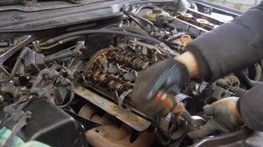 Tamirci, emniyet millerini açmak için ingiliz anahtarı kullanıyor ve açık araba motorundaki vanalara basıyorlar. Görünür bileşenler arasında vanalar, silindir başı ve garaj ortamındaki çeşitli araçlar yer almaktadır.