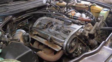 Araba tamircisi eldiven giyerken buharlı motor bölümünü inceliyor. Araç kullanılıyor, motor sorunları için mekanik denetimler, potansiyel aşırı ısınma sorunları ele alınıyor
