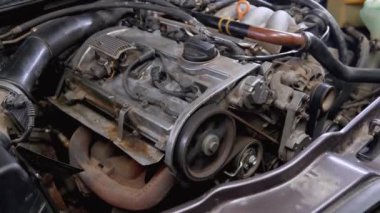 Araba tamircisi eldiven giyerken buharlı motor bölümünü inceliyor. Araç kullanılıyor, motor sorunları için mekanik denetimler, potansiyel aşırı ısınma sorunları ele alınıyor