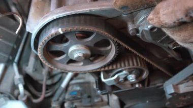 Araba motorunun zamanlayıcı kayışını değiştiren tamircinin elleri yakın plan. Tamirci, dişlideki zamanlayıcı kemeri izlerine işaret ediyor. Lto pistonun tam ortasını ayarlıyor..