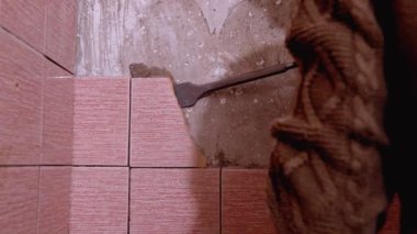 İnşaat işçisi kaya matkabını kullanarak banyo duvarındaki fayansları söküyor. Duvar kısmen yıkılmış, alttaki betonu ortaya çıkarıyor.