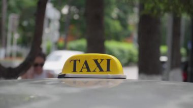 Araç çatısında parlayan ışıklı sarı taksi tabelası, şehir caddesinde gündüz vakti bulanık yaya hareketinin ortasında yolcuların hazır olduğunun sinyalini veriyor.