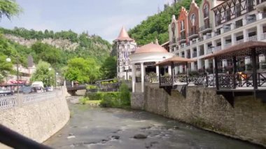 Borjomi şehir merkezi, otelin balkonları ve akan nehir manzaralı, yemyeşil ve taştan setle çevrili bir manzarasını gösteriyor.