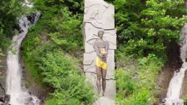 Borjomi, Gürcistan 'daki şelalede Prometheus anıtı. Tanrı 'nın heykeli, yemyeşil bitki örtüsüyle çevrili.