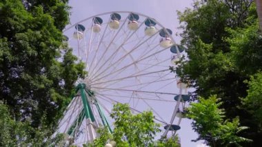 Parlak dönme dolap, parlak yaz güneşi altında Georgia Borjomi 'de neşeli bir eğlence parkında yeşil ağaçların arkasında yavaşça dönüyor..