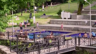 İnsanlar, Borjomi, Gürcistan 'da yeşil ağaçlar ve çimlerle çevrili yaz havasının keyfini çıkararak, açık hava termal havuzunda dinleniyor..