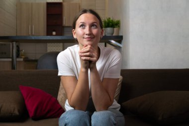 Elleri dua ederken kanepede oturan genç bir kadın. İnancında teselli ve rehberlik ararken yüzünü umut ve sadakati ifade ediyor.