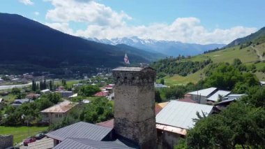 Gürcistan 'ın Svaneti bölgesinin tarihi Mestia köyünde, antik Svaneti mimarisinin yüksek ortaçağ taş yapıları resim dağlarının zeminine karşı yükseliyor. Kuledeki adam. İHA 'dan ateş ediliyor.