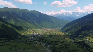 Beyaz bulutlar nazikçe yükselen dağ zirvesini okşar, aşağıdaki parlak yeşil vadiye gölgeler bırakır, toprak yol manzaranın içinden eser. İHA 'dan ateş ediliyor.