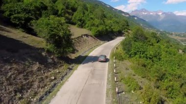 Yeşil vadiden geçen dolambaçlı dağ yolu, parlak yaz güneşi altında manzaralı yoldan geçen arabalar, engin manzaralar ve Drone 'un doğal dağlık arazisi.