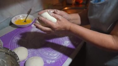 Profesyonel fırıncı, hamuru nazikçe mor silikon paspasın üzerine katlıyor, yumurta çırpıyor, mutfak çalışma alanında hassas mutfak tekniğini gösteriyor.