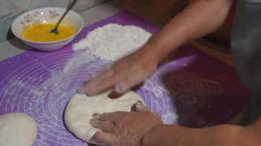 Profesyonel fırıncı, hamuru nazikçe mor silikon paspasın üzerine katlıyor, yumurta çırpıyor, mutfak çalışma alanında hassas mutfak tekniğini gösteriyor.