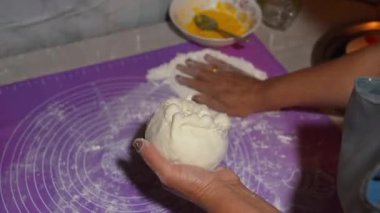 Profesyonel fırıncı, hamuru nazikçe mor silikon paspasın üzerine katlıyor, yumurta çırpıyor, mutfak çalışma alanında hassas mutfak tekniğini gösteriyor.