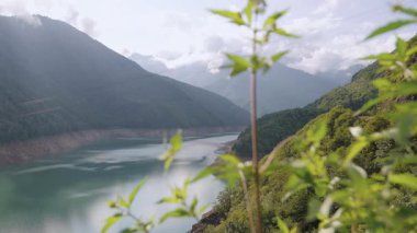 Gürcistan 'ın Svaneti bölgesindeki Enguri Nehri manzarası yemyeşil dağlar ve tepeler arasına yerleşmiş, açık gökyüzünün altında hafifçe dalgalanan yeşilliklerle