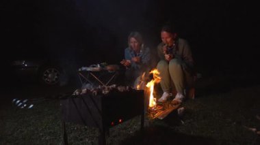 Kızların iki kız arkadaşı ateşte sıcaklığın ve yemeğin tadını çıkarıyor. Açık hava sahnesi, sıcak bir atmosferi ateş ve rahat bir akşam yemeği ile yakalar.
