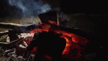 Parlayan kamp ateşi yoğun bir şekilde yanıyor, karanlığın ortasına sıcak bir ışık tutuyor, çatırdayan odunlar ve canlı közler yayıyor kırsal vahşi ortam yayıyor.