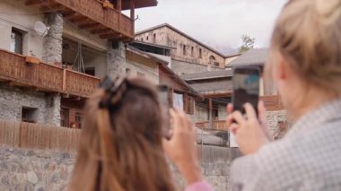 İki turist, geleneksel köyde akıllı telefonlar kullanarak, kültürel mirası ve manzaralı güzelliği yakalayarak büyüleyici kırsal mimarinin fotoğraflarını çekiyor.