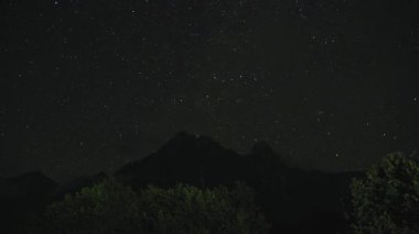 Gece vakti ortaya çıkan hareketli bulutlar dağlık orman manzarasının üzerindeki yıldızlı gökyüzünü yavaş yavaş örterek dramatik siluetler ve atmosferik manzaralar yaratıyor.