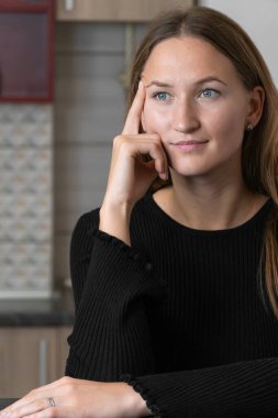 Genç bir kadın mutfak masasında oturuyor ve elini yüzüne koyup başka tarafa bakıyor. Hoş bir şeyin hayalini kuruyor, yeni dairesinin keyfini çıkarıyor. Dikey fotoğraf