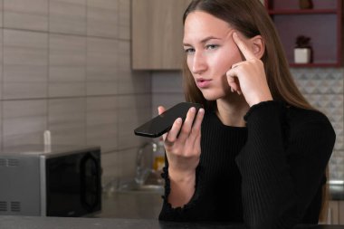 Mutfakta akıllı telefon kullanan, sesli mesaj kaydeden ya da hoparlörden telefonla konuşan, modern iletişim teknolojisinin keyfini çıkaran genç bir kadın.