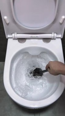 Profesyonel hademe, beyaz seramik klozeti iyice temizler. İnatçı kiri ve inatçı kiri ortadan kaldırmak için iç yüzeyleri siyah plastik fırçayla ovalar. Yavaş çekim dikey video