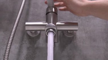 Profesyonel tesisatçı krom duş musluğunu manipüle ederek su basıncını ölçüyor. Ev bakımı sırasında modern gri kiremitli banyodaki akış dinamiklerini değerlendiriyor.