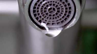 Musluğun koyu gri metal oluğundan su damlacıkları oluşur ve düşer, iç ortamlardaki çevresel su atıkları ve kaynak koruma sorunlarını vurgular