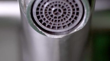 Musluğun koyu gri metal oluğundan su damlacıkları oluşur ve düşer, iç ortamlardaki çevresel su atıkları ve kaynak koruma sorunlarını vurgular