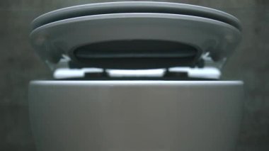 Gösterişli klozet oturağı yavaşça koyu gri fayansların üzerine konuyor, çağdaş banyo tasarımını minimalist siyah aksesuarlarla renklendiriyor.