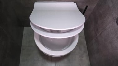 Hijyenik beyaz tuvalet kapağı zarif modern banyoda koyu gri seramik fayanslarla ve minimalist siyah tuvalet fırçasıyla nazikçe indirir.