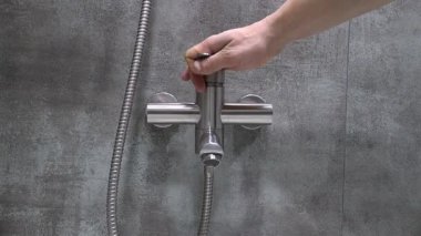 Profesyonel tesisatçı krom duş musluğunu manipüle ederek su basıncını ölçüyor. Ev bakımı sırasında modern gri kiremitli banyodaki akış dinamiklerini değerlendiriyor.
