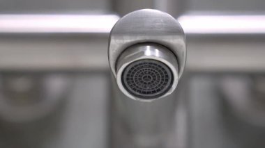 Musluğun koyu gri metal oluğundan su damlacıkları oluşur ve düşer, iç ortamlardaki çevresel su atıkları ve kaynak koruma sorunlarını vurgular